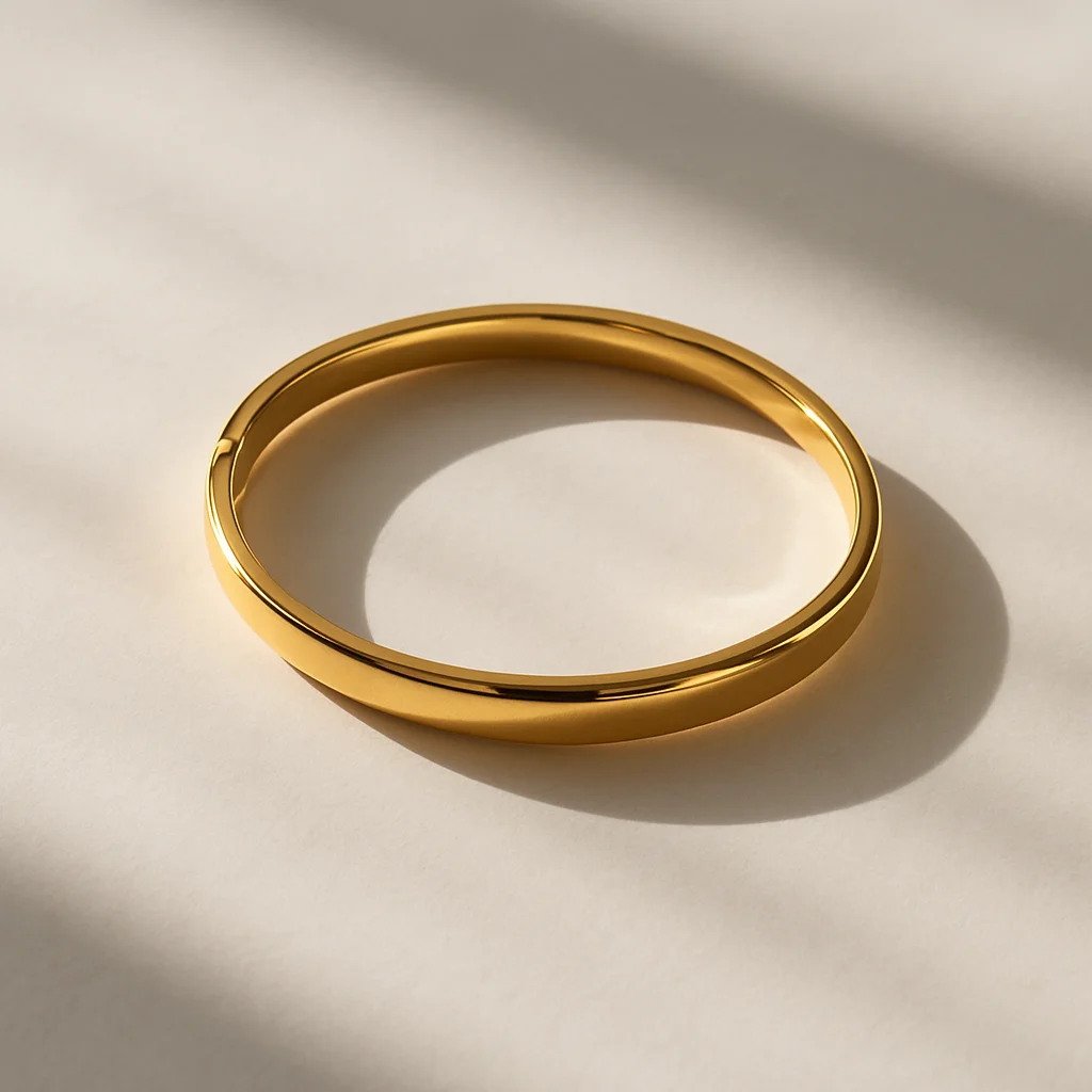 A close-up flat lay of three stacked gold bracelets — a delicate vermeil chain, a solid 14k Cuban link, and a wide cuff — resting on warm cream linen beside a hallmark stamp reference card